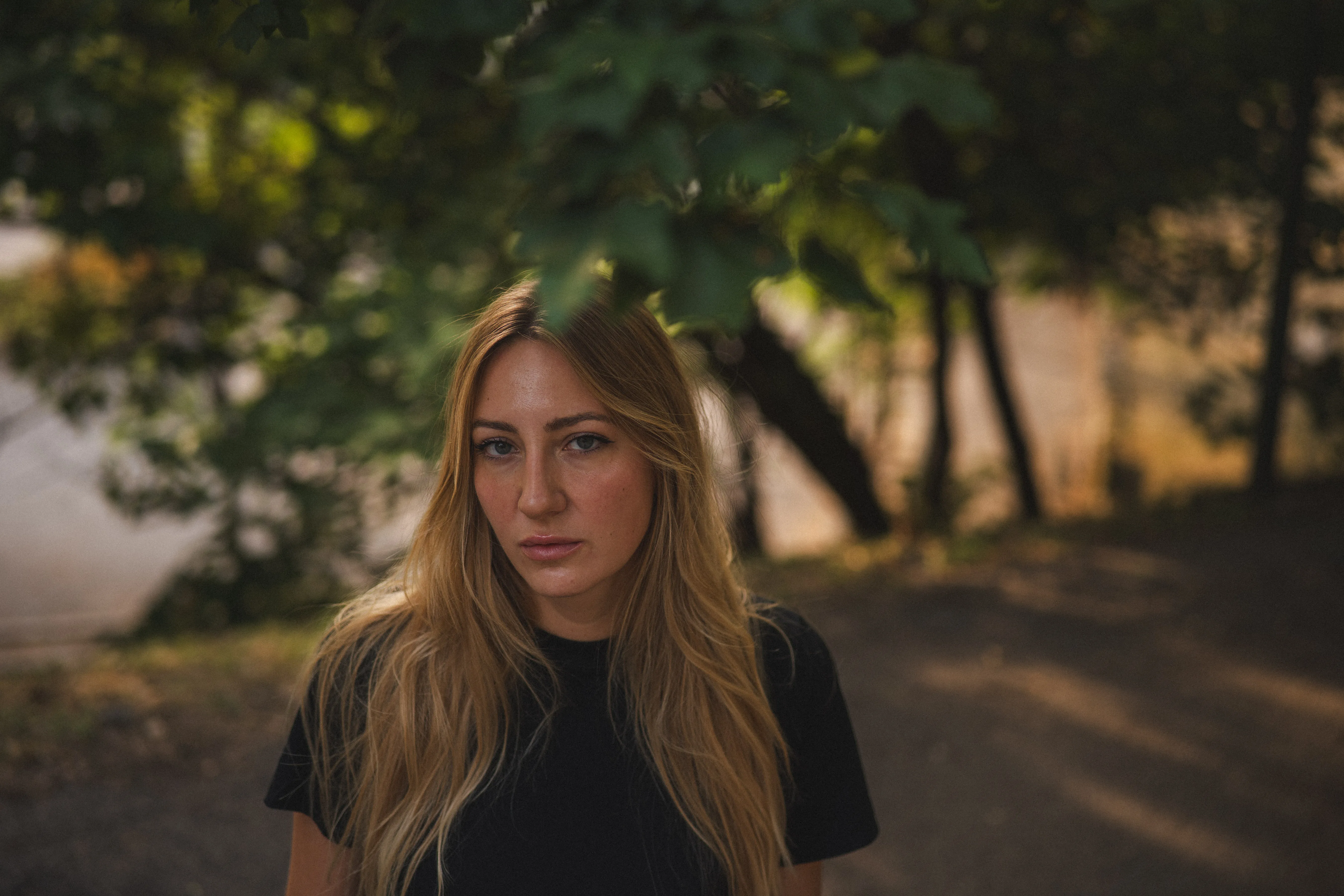 portrait of an italian woman with long blonde hair in le colombare park, verona, italy, at golden hour: eyes closed in the sun, under the leaves, on a park bench (3)
