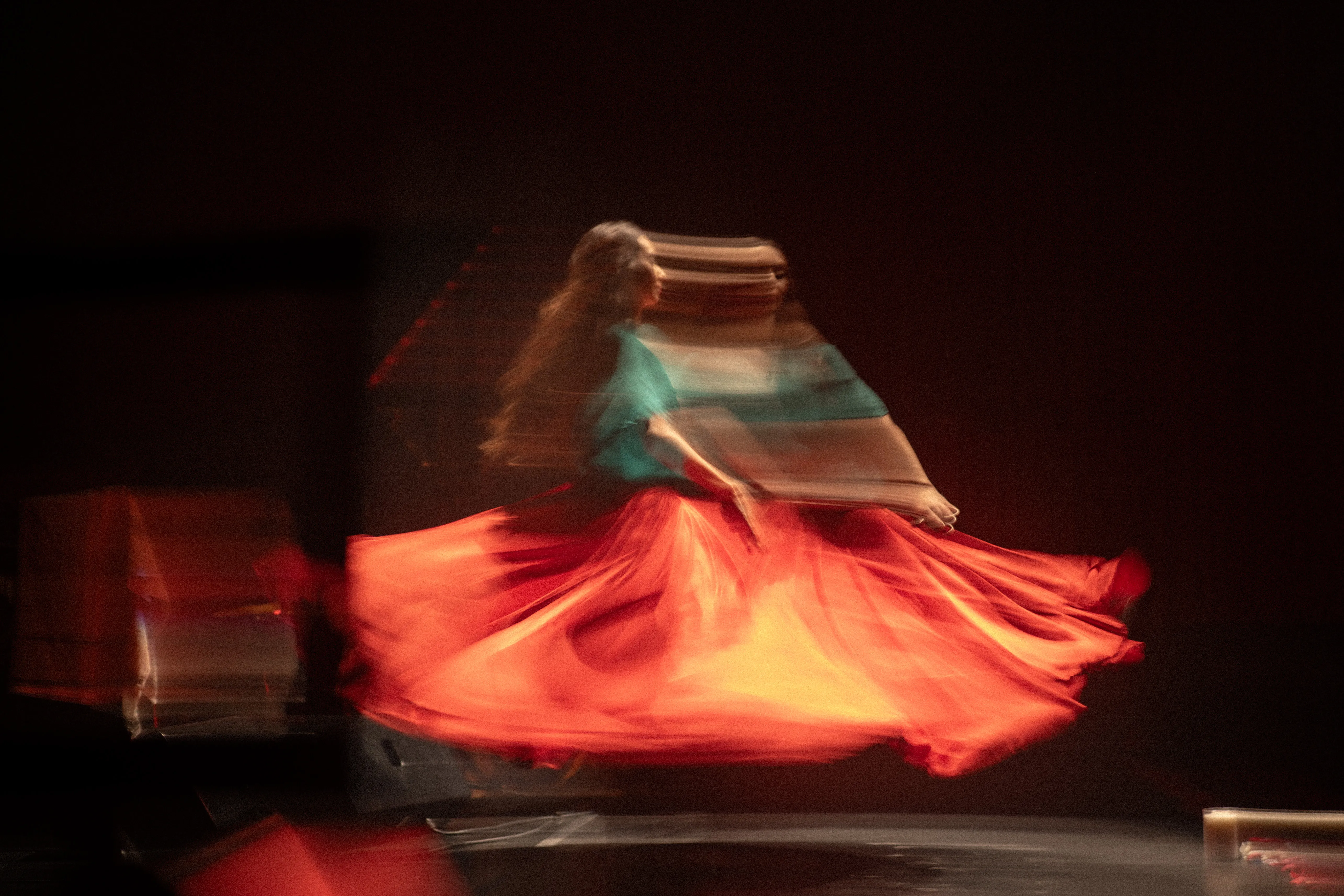 claudia llanos, rajasthani dancer from mexico, caught mid-turn in a long exposure, orange skirt, dancing to xarab at centro cultural de españa, mexico city