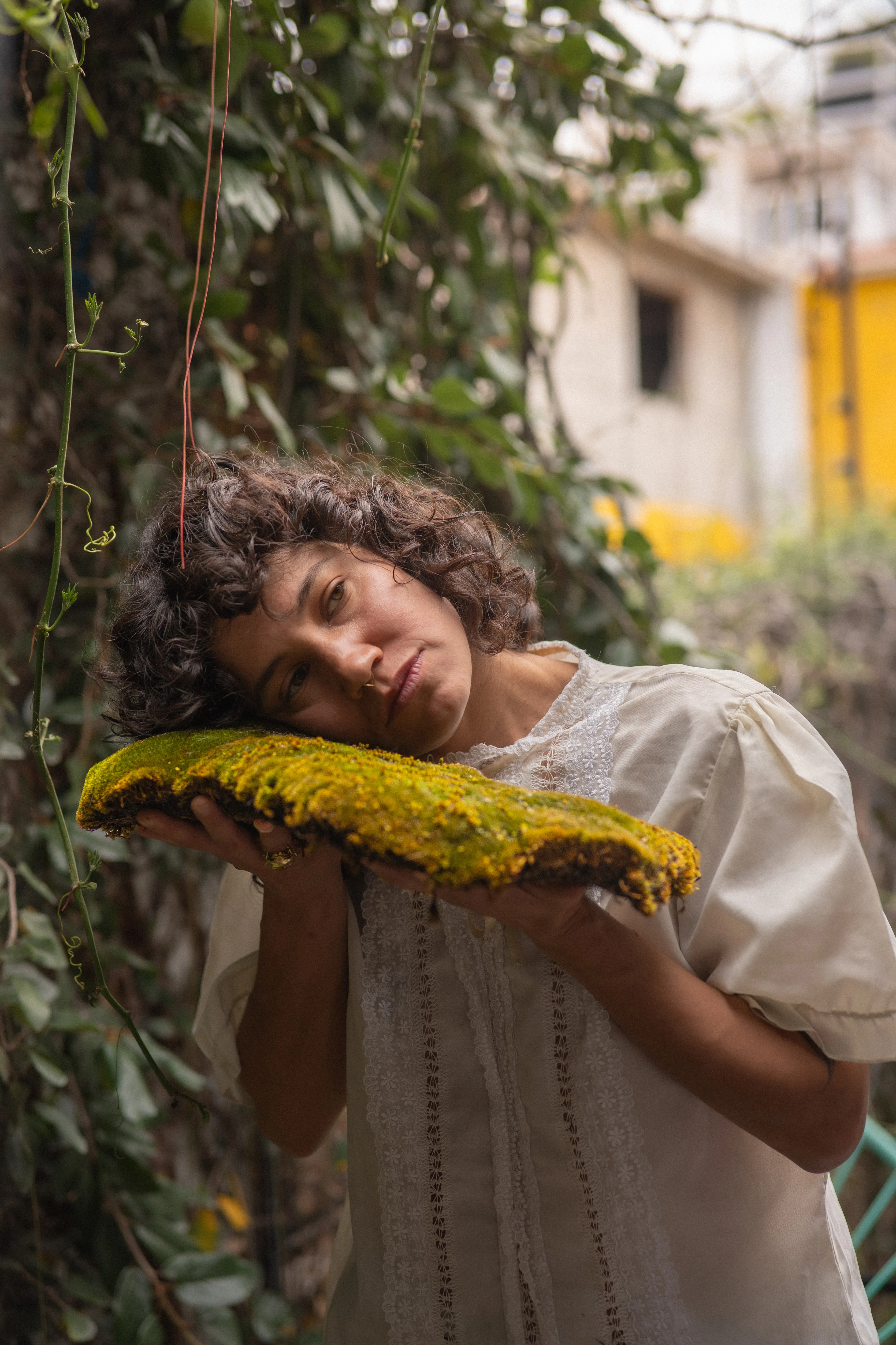 dark curly-haired woman with a septum piercing holding moss on a terrace in mexico city, intense gaze (2)